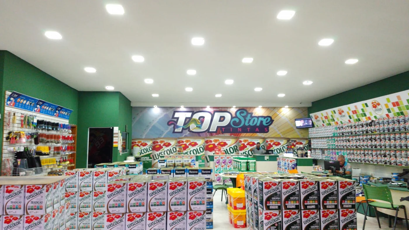 Interior da loja Topstore Tintas em Americana, com parede de amostras de cor e produtos Lukscolor